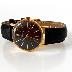 May include: A gold-tone wristwatch with a black face and gold-tone hands. The watch has a black leather band.