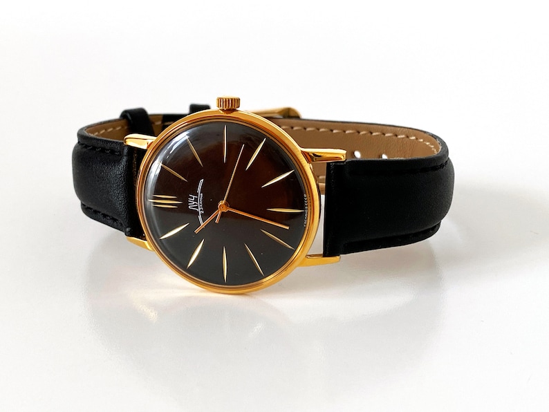 May include: A gold-tone wristwatch with a black face and gold-tone hands. The watch has a black leather band.