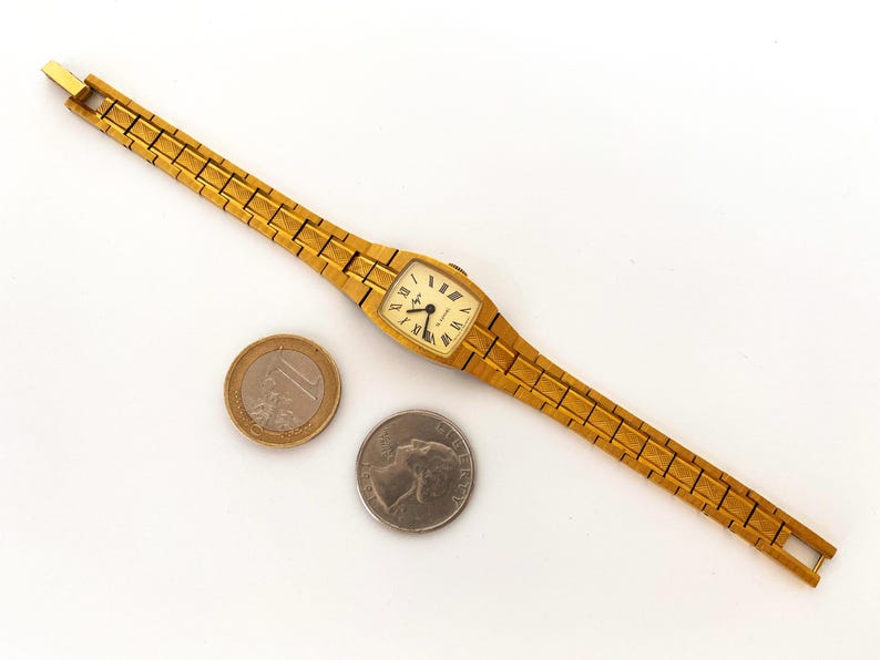 K&ouml;nnte beinhalten: Eine goldfarbene Armbanduhr mit quadratischem Zifferblatt und einem goldfarbenen Metallband. Das Zifferblatt hat schwarze r&ouml;mische Ziffern als Stundenmarkierungen und schwarze Zeiger.