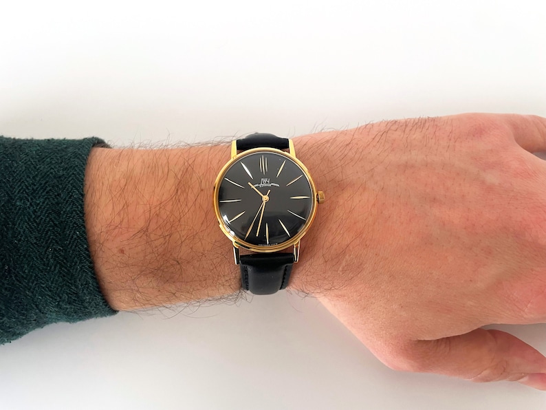 May include: A gold-tone wristwatch with a black face and black leather band. The watch face has gold-tone hands and Roman numeral hour markers.