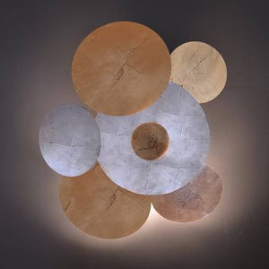 Könnte beinhalten: Eine Wandleuchte im modernen Design mit mehreren überlappenden Kreisen in Gold- und Silbertönen.