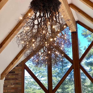 Pu&ograve; includere: Un grande lampadario rustico fatto di rami intrecciati con luci bianche calde. Il lampadario &egrave; appeso a un soffitto in legno con una grande finestra dietro.