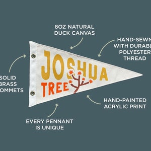 May include: A white pennant flag with the words "Joshua Tree" in yellow and orange lettering. The flag is hand-painted with acrylic paint and has solid brass grommets. It is made from 8 oz natural duck canvas and hand-sewn with durable polyester thread.
