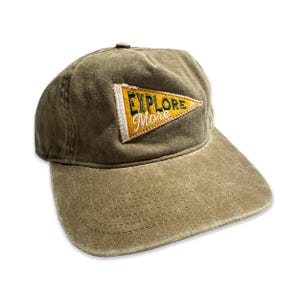 May include: A green and yellow embroidered patch on a brown baseball cap reads "Explore More".