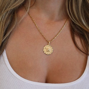 May include: A gold chain necklace with a round pendant featuring an angel design.