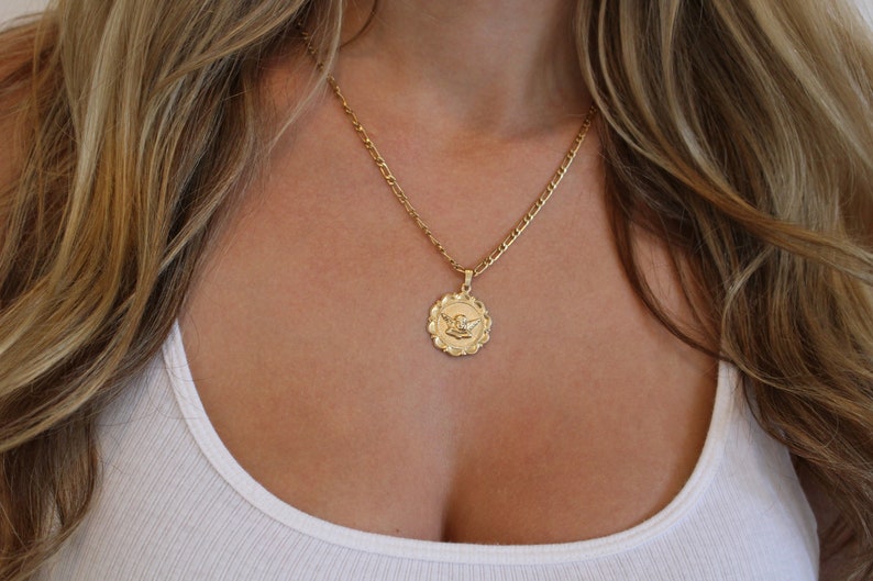 May include: A gold chain necklace with a round pendant featuring an angel design.
