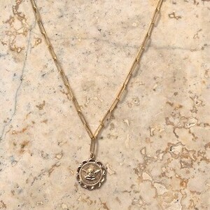 May include: A gold chain necklace with a round pendant featuring a detailed angel design.