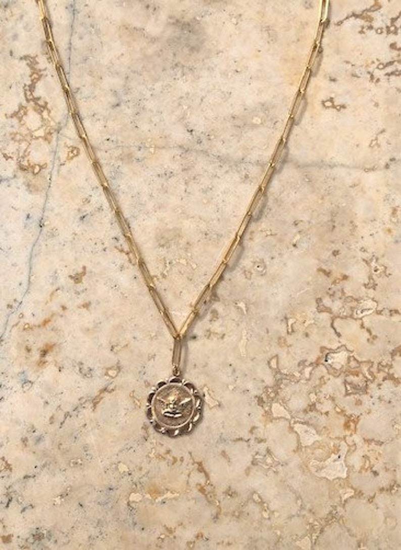 May include: A gold chain necklace with a round pendant featuring a detailed angel design.