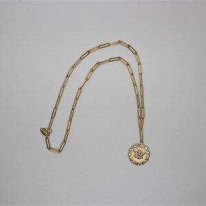 May include: A gold chain necklace with a gold pendant featuring an angel with wings. The pendant is round and has a textured edge.