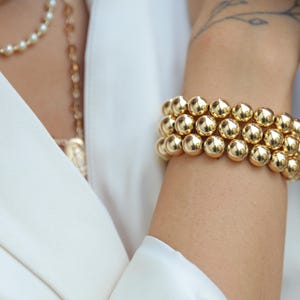 May include: A gold bracelet made of large, round beads. The bracelet is worn on a person's wrist.