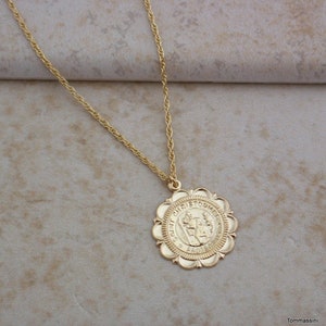 May include: A gold chain necklace with a round pendant featuring a depiction of Saint Christopher. The pendant has a scalloped edge and the words "Saint Christopher" are inscribed around the image.