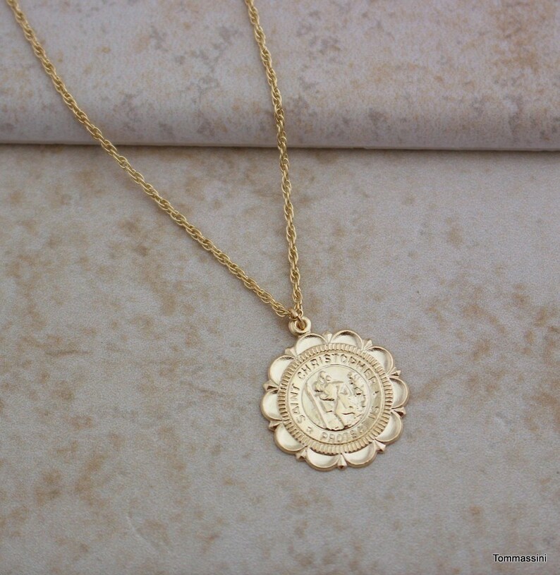 May include: A gold chain necklace with a round pendant featuring a depiction of Saint Christopher. The pendant has a scalloped edge and the words "Saint Christopher" are inscribed around the image.
