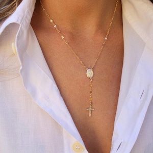 Puede incluir: Un collar de cadena dorada con un peque&ntilde;o colgante ovalado y un dije de cruz.