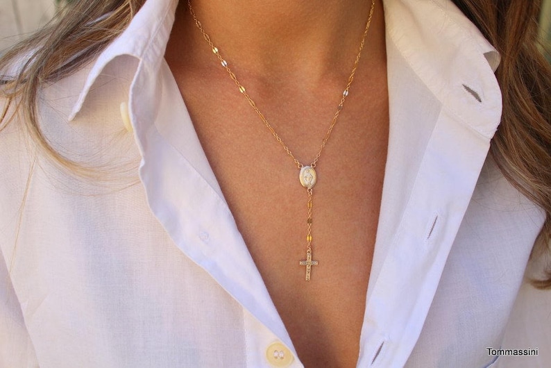 Puede incluir: Un collar de cadena dorada con un peque&ntilde;o colgante ovalado y un dije de cruz.