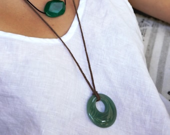 May include: A layered necklace set featuring three strands of green gemstone pendants. The top strand has small beads, the middle has a large oval stone, and the bottom has a large, open circle pendant, all on brown cords.