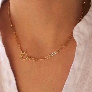 Può includere: Una collana a catena dorata con chiusura a levetta. La catena è composta da rettangoli collegati.