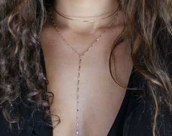 Könnte beinhalten: Eine goldene mehrreihige Halskette mit einer langen, zarten Kette und einer kürzeren, dickeren Choker-Kette. Die Halskette wird von einer Person mit langen, lockigen braunen Haaren getragen.