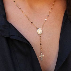 Puede incluir: Un collar de cadena de oro con un peque&ntilde;o colgante ovalado que presenta una imagen religiosa y un peque&ntilde;o dije de cruz.