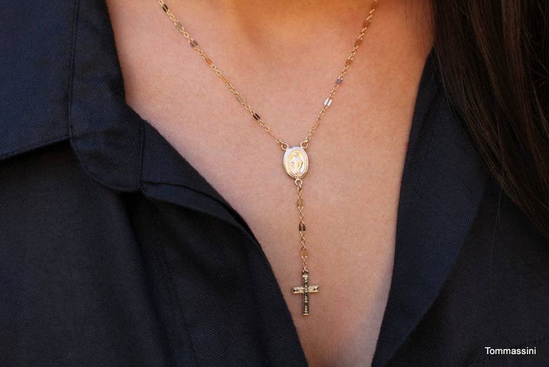 Puede incluir: Un collar de cadena de oro con un peque&ntilde;o colgante ovalado que presenta una imagen religiosa y un peque&ntilde;o dije de cruz.