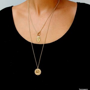 May include: Two gold chain necklaces with pendants. The top necklace has a toggle clasp and a small oval pendant with a religious figure. The bottom necklace has a larger round pendant with a detailed design.