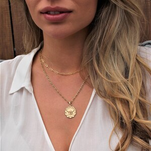 May include: A gold chain necklace with a delicate pendant featuring a stylized angel design. The necklace is layered with a second, thinner chain.