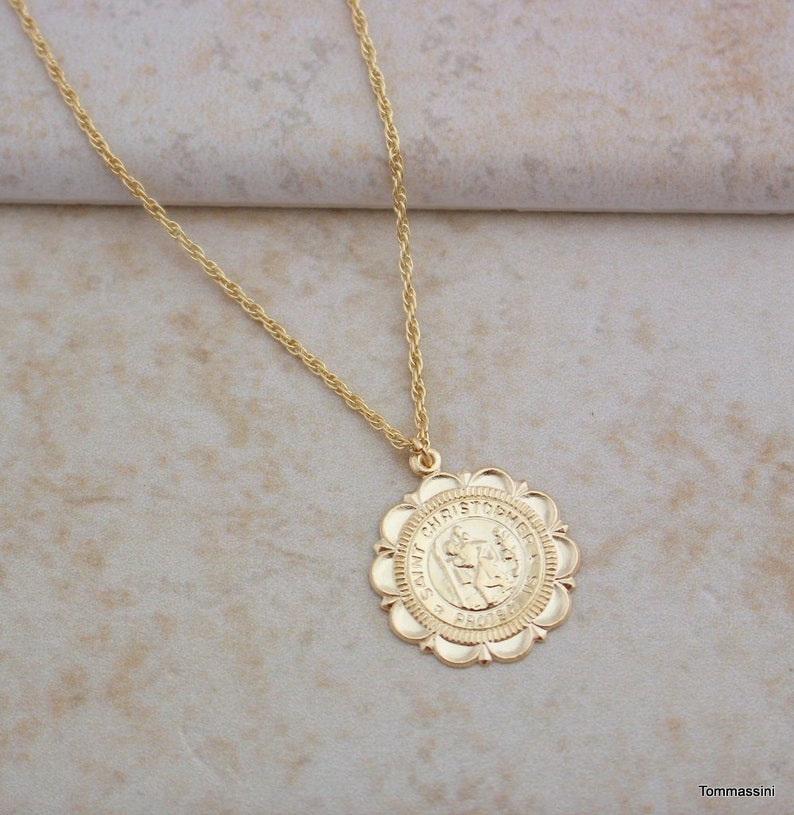 May include: Gold chain necklace with a round pendant featuring a depiction of Saint Christopher. The pendant has a scalloped edge and the words "Saint Christopher" are inscribed around the image.