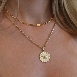 May include: A gold chain necklace with a delicate chain and a pendant featuring a small angel design.