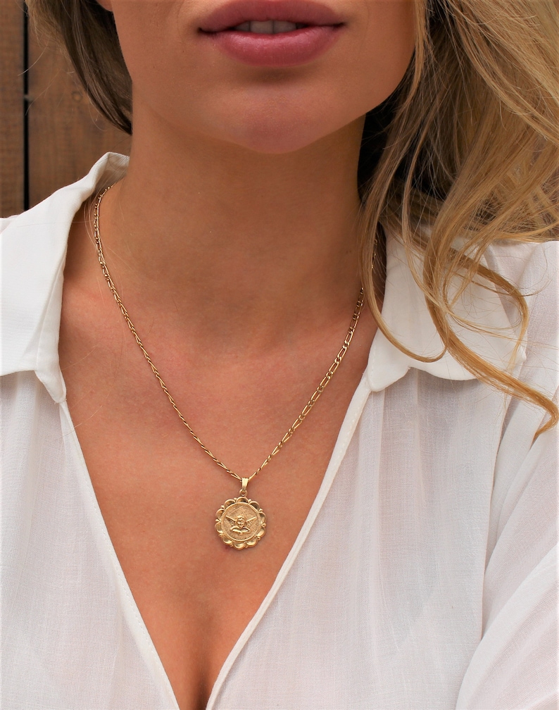 May include: A gold chain necklace with a round pendant featuring an angel design.