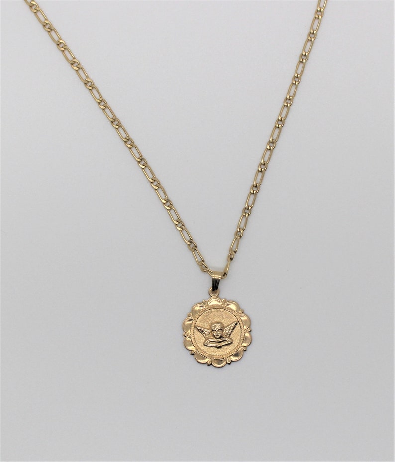 May include: A gold chain necklace with a round pendant featuring a cherub with wings. The pendant has a scalloped edge.