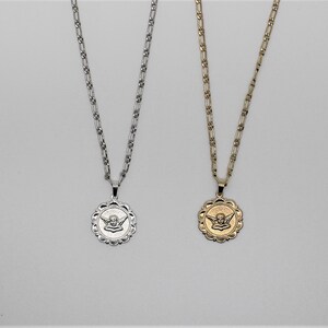 May include: Two silver and gold necklaces with angel pendant charms. The pendants are round and feature a detailed angel design. The chains are both silver and gold.