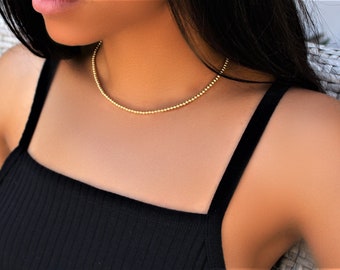 May include: A gold beaded necklace on a person wearing a black tank top.