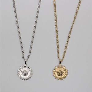 May include: Two silver chains with angel medallions. The medallions are round and have a detailed design of an angel with wings. One chain is silver and the other is gold.