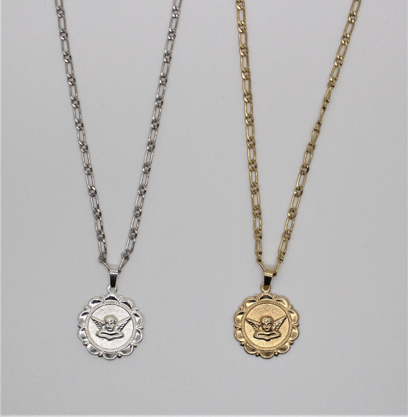 May include: Two silver chains with angel medallions. The medallions are round and have a detailed design of an angel with wings. One chain is silver and the other is gold.