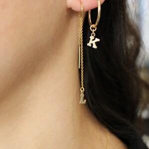 May include: Gold hoop earrings with a dangling chain and letter charms. The charms spell out the letters "K" and "L".