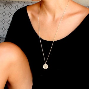 May include: A woman wearing a black scoop neck shirt with a silver chain necklace and a small round pendant.