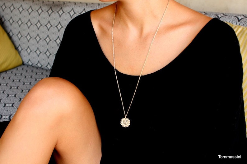 May include: A woman wearing a black scoop neck shirt with a silver chain necklace and a small round pendant.