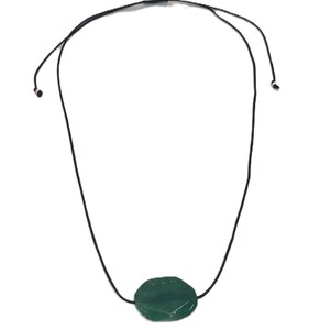 May include: A necklace featuring a dark green, oval-shaped gemstone pendant. The pendant is suspended from a black cord that can be adjusted for length. The gemstone has a faceted surface, catching the light. The necklace is displayed against a white background.