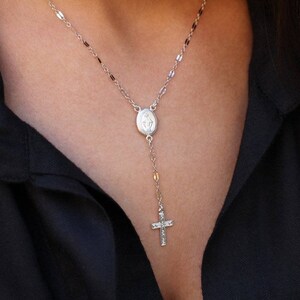Puede incluir: Un collar de cadena de plata con un peque&ntilde;o colgante ovalado y un dije de cruz.