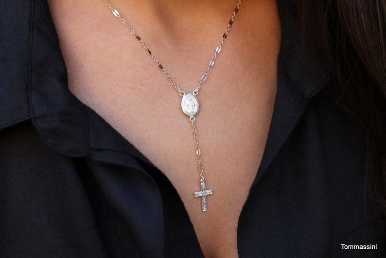 Puede incluir: Un collar de cadena de plata con un peque&ntilde;o colgante ovalado y un dije de cruz.