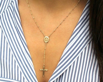 May include: A gold chain necklace with a small oval pendant featuring a religious image and a cross charm.