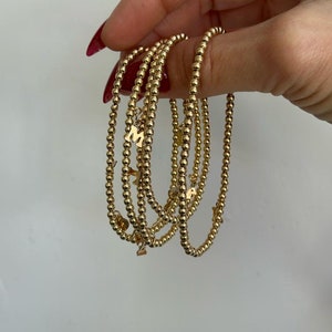 May include: A set of five gold beaded bracelets with letter charms. The charms spell out the word "MAMA".