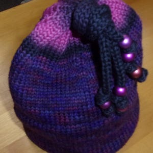May include: A purple and black knitted hat with a black crocheted tassel and purple beads.