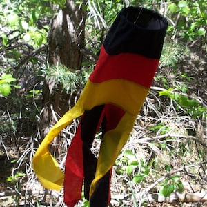 Puede incluir: Un streamer de tela negro, rojo y amarillo cuelga de una rama de árbol. El streamer tiene forma de lágrima y tiene una cola larga y fluida.