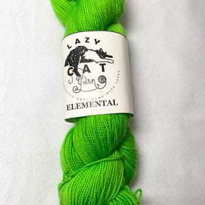 May include: A skein of bright green yarn with a white label that reads "LAZY CAT Yarn" and "ELEMENTAL" in black text. The label also features a black and white illustration of a cat.