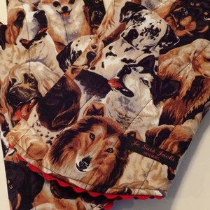 May include: A pair of brown and beige oven mitts with a quilted design featuring a variety of dog breeds. The mitts have a red scalloped edge and a black label that reads "Je Suis Jacki Originals".