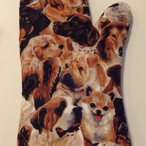 May include: A brown and white oven mitt with a colorful pattern of different dog breeds. The mitt has a red scalloped edge.