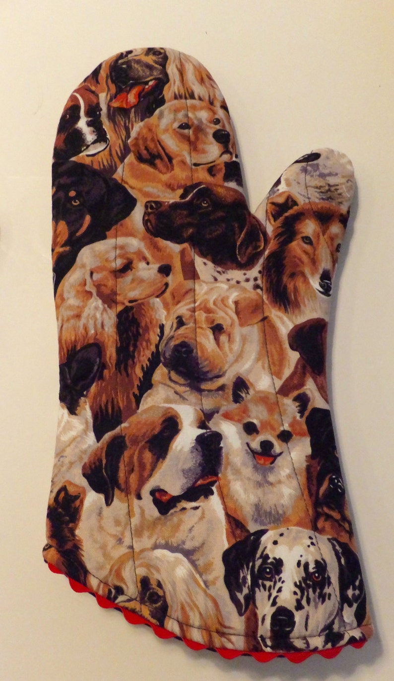 May include: A brown and white oven mitt with a colorful pattern of different dog breeds. The mitt has a red scalloped edge.