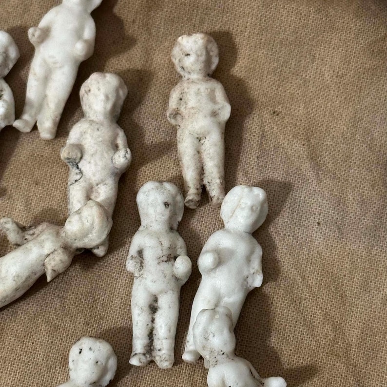 Pu&ograve; includere: Una collezione di piccole bambole antiche in biscuit in varie pose. Le bambole sono principalmente bianche con qualche scolorimento, e sono disposte su una superficie dai toni neutri. Le bambole sono in una variet&agrave; di pose, alcune in piedi e altre sdraiate.