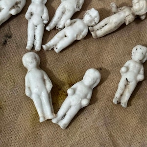 Pu&ograve; includere: Una collezione di piccole figure di bambole in porcellana bianca. Le bambole sono in varie pose, alcune in piedi e altre sdraiate. La porcellana ha un aspetto leggermente invecchiato, con qualche scolorimento. Le bambole sono probabilmente vintage o antiche.