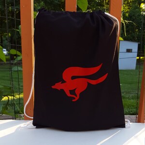 Könnte beinhalten: Eine schwarze Kordeltasche mit einem roten Star Fox Logo. Das Logo zeigt einen roten Fuchs, der mit ausgebreiteten Schwanz rennt.